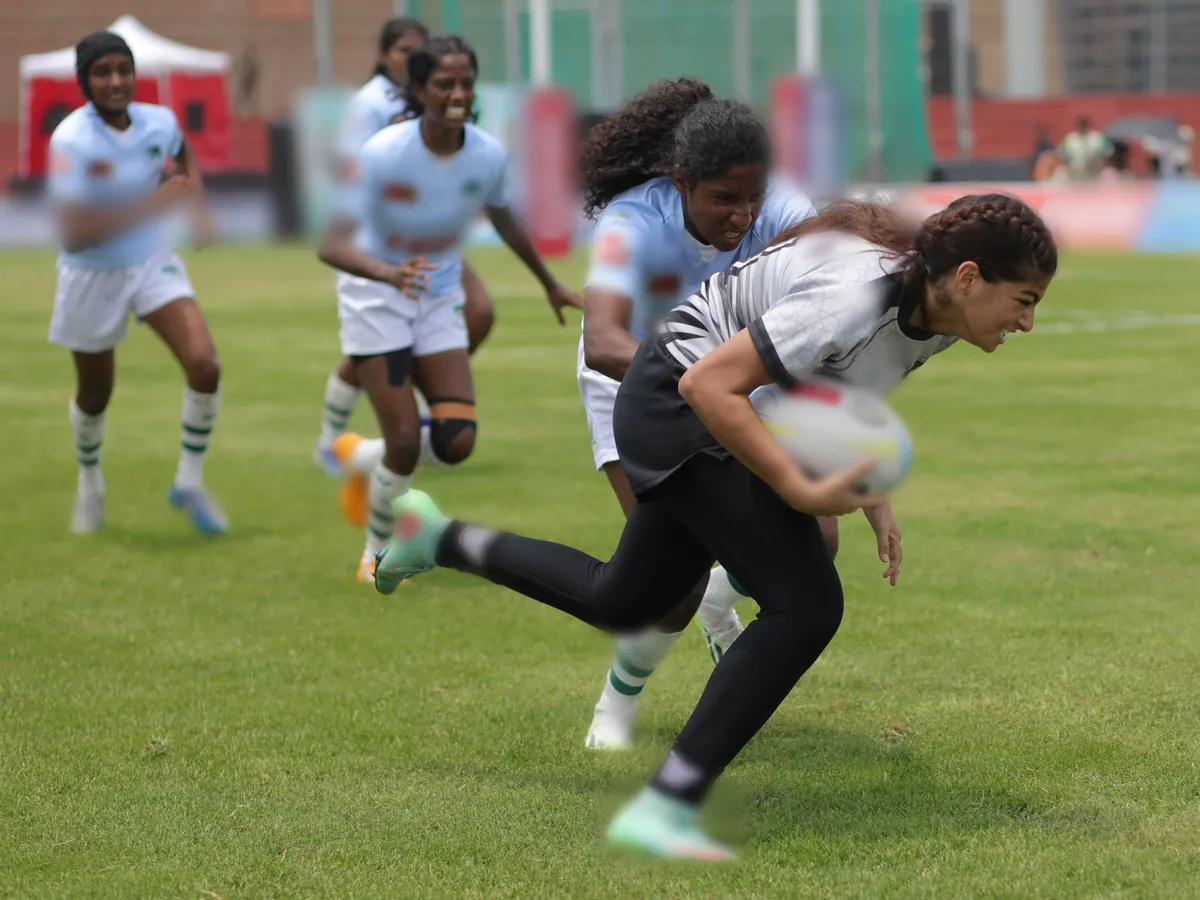 A women's sevens rugby player carries the ball past a tackler