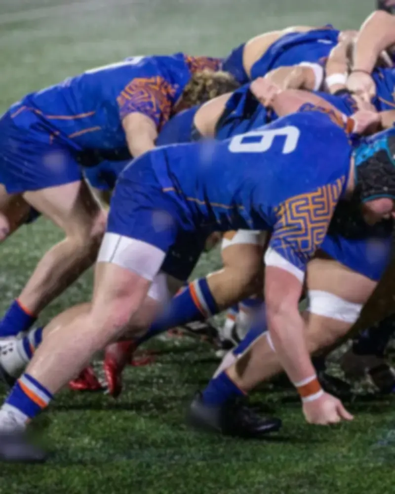 Men's rugby forwards bound together in a scrum on a wet night